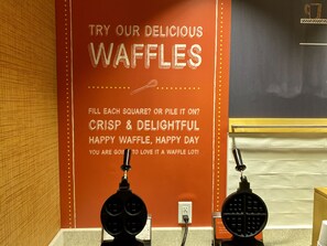 A wall with a waffle advertisement and two waffle makers. - Hampton Inn & Suites Deland (DeLand)