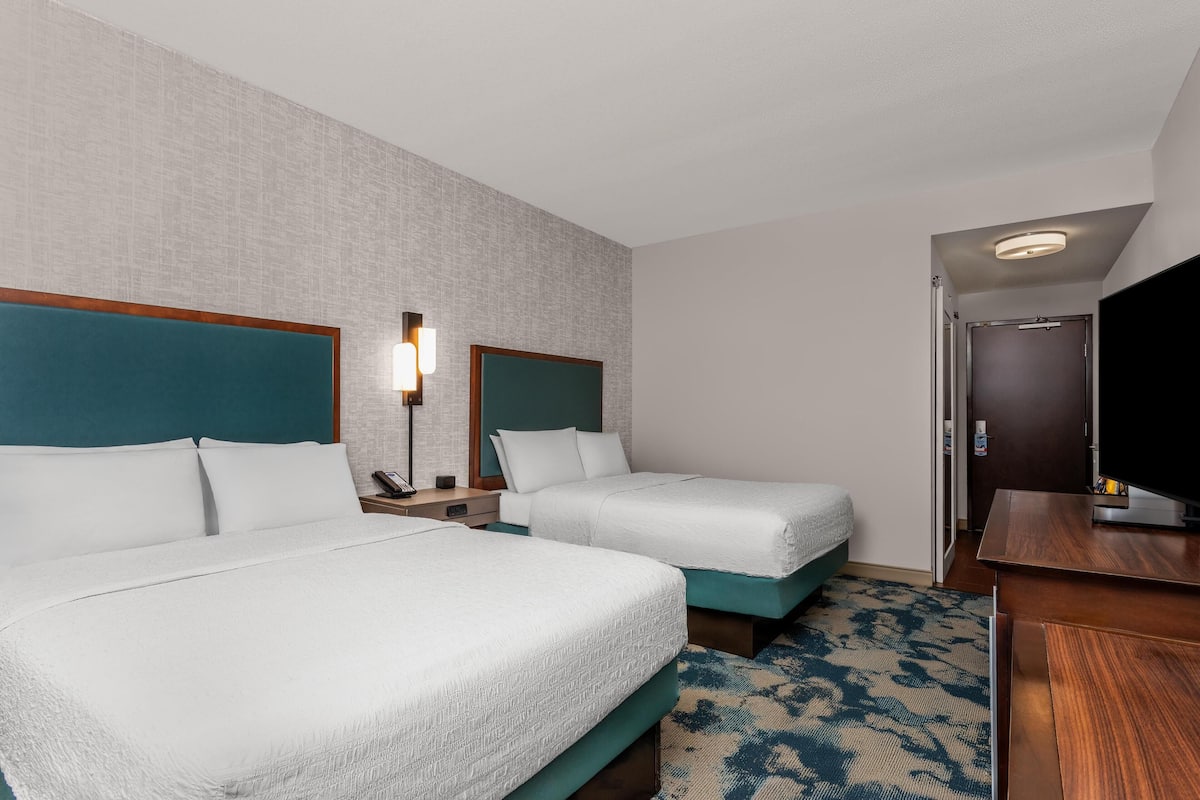 A hotel room with two beds, a desk, a TV, and a door leading to a bathroom.