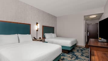 A hotel room with two beds, a desk, a TV, and a door leading to a bathroom.