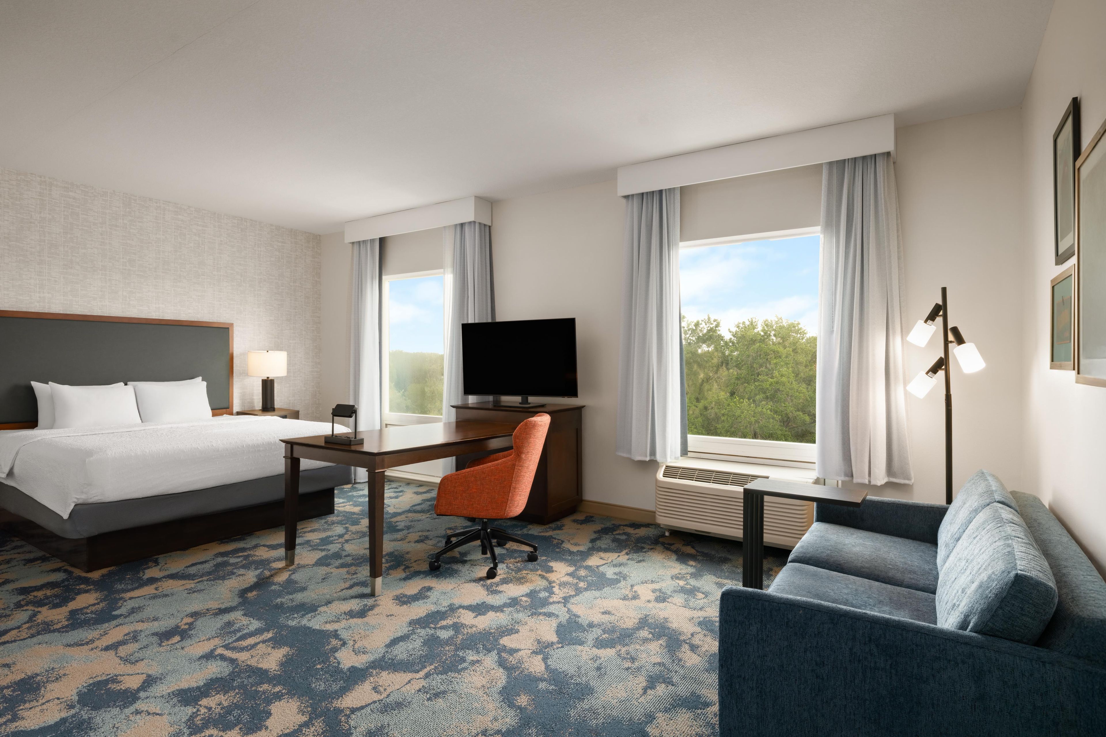 Hotellihuone, jossa on sänky, työpöytä, tuoli, televisio ja sohva.