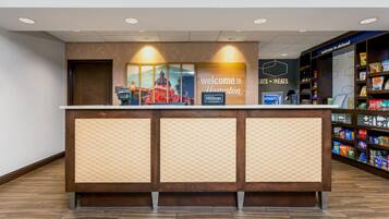 A hotel reception desk with a 'Welcome to Hampton' sign, a 'Cats & Treats' sign, and a snack bar with various snacks.