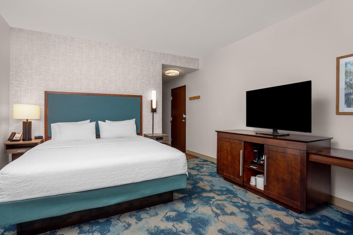 A hotel room with a bed, a TV, a desk, and a lamp.