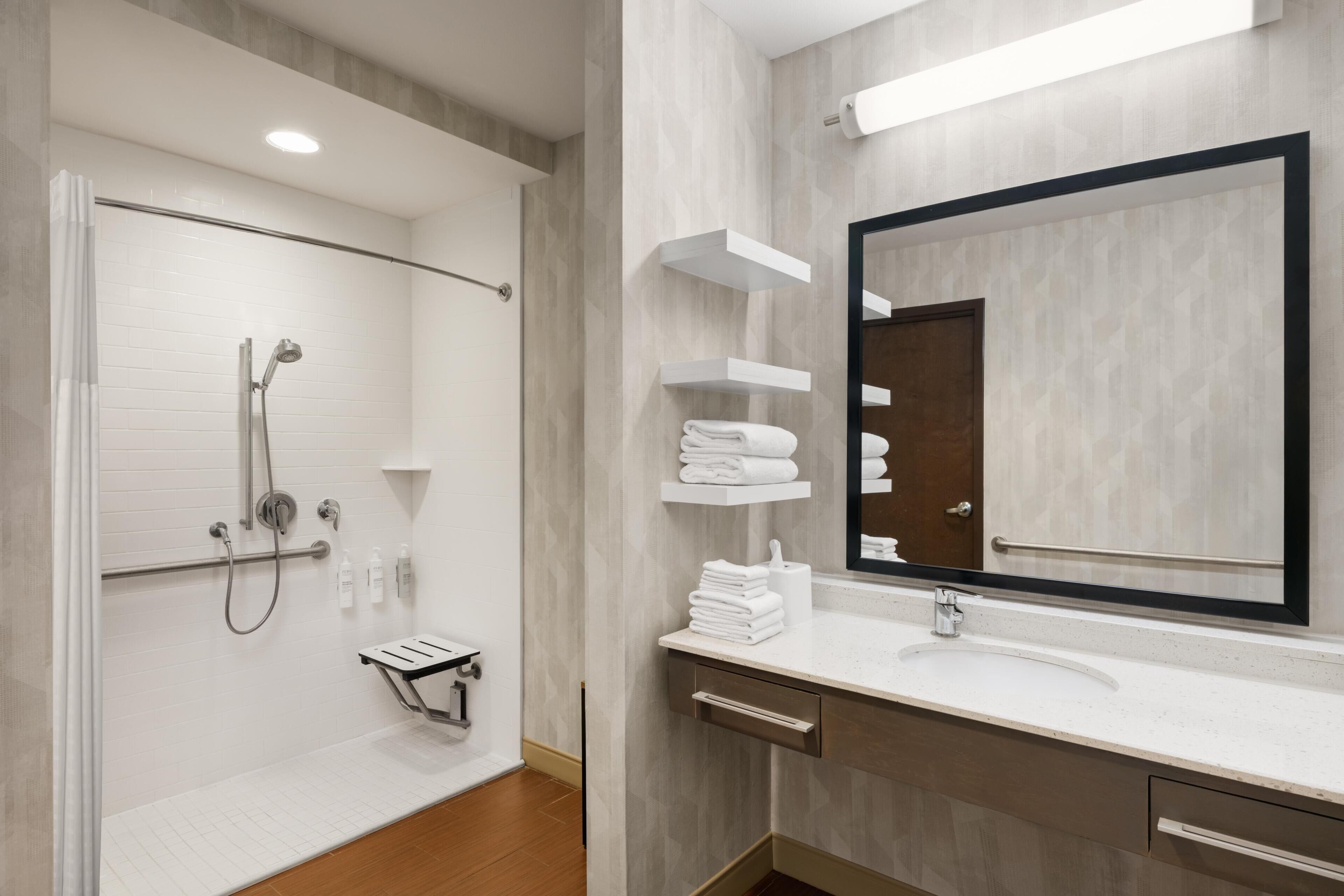Un baño moderno con cabina de ducha, tocador con espejo y toallas ordenadamente dobladas.