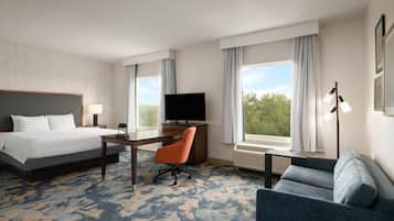 A hotel room with a bed, a desk, a chair, a television, and a sofa.