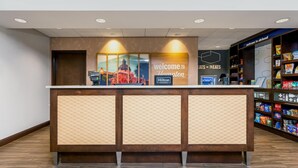 Een hotel receptie met een 'Welcome to Hampton' bord, een 'Cats & Treats' bord, en een snackbar met diverse snacks.
