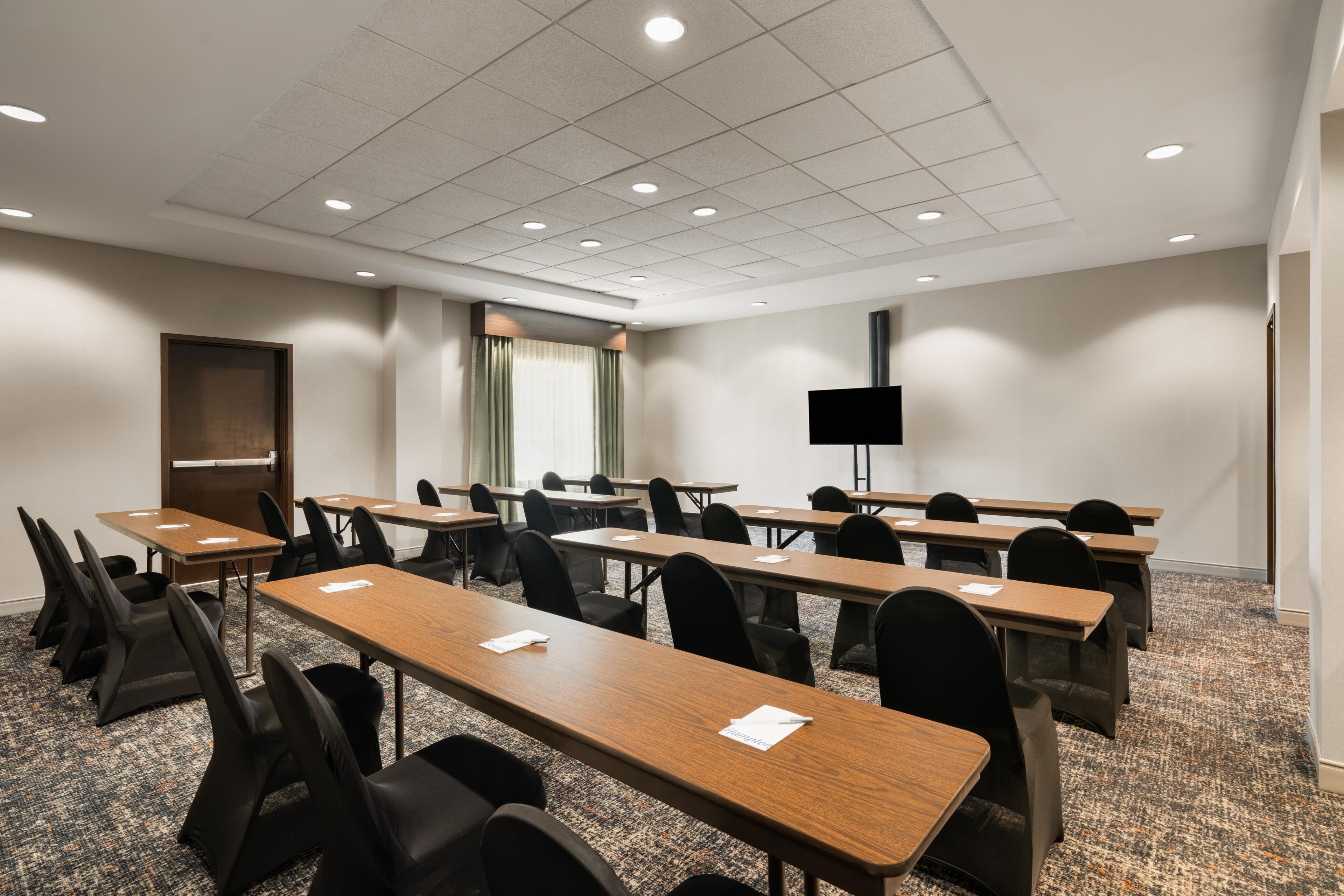 A conference room with multiple tables and chairs, a flat-screen TV, and a door.