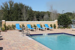 Una piscina con sillas reclinables azules y un patio de ladrillo.