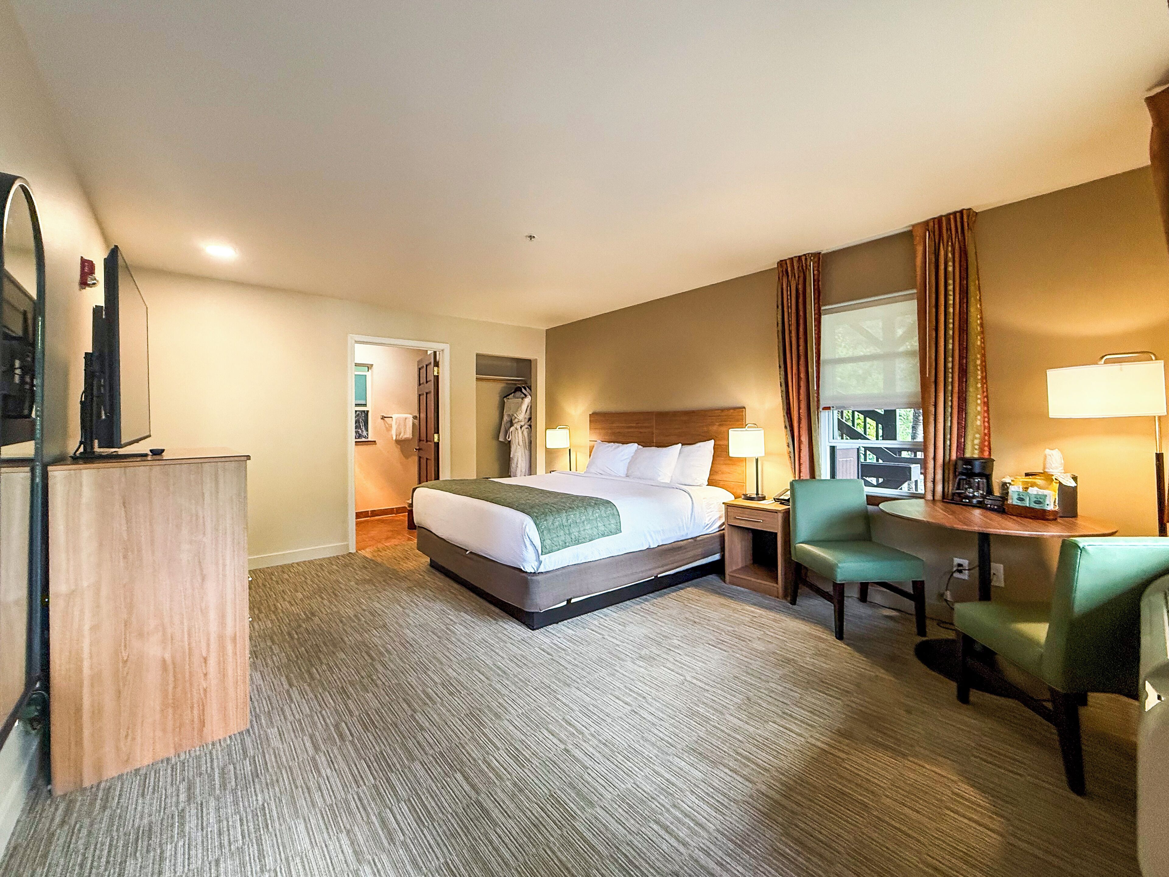 Habitación de hotel con cama, escritorio con silla, televisión y baño visible a través de una puerta abierta.