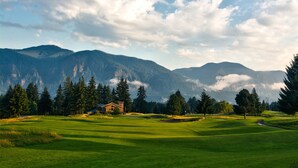 Een golfbaan met een huis op de achtergrond, omgeven door bergen en bomen.