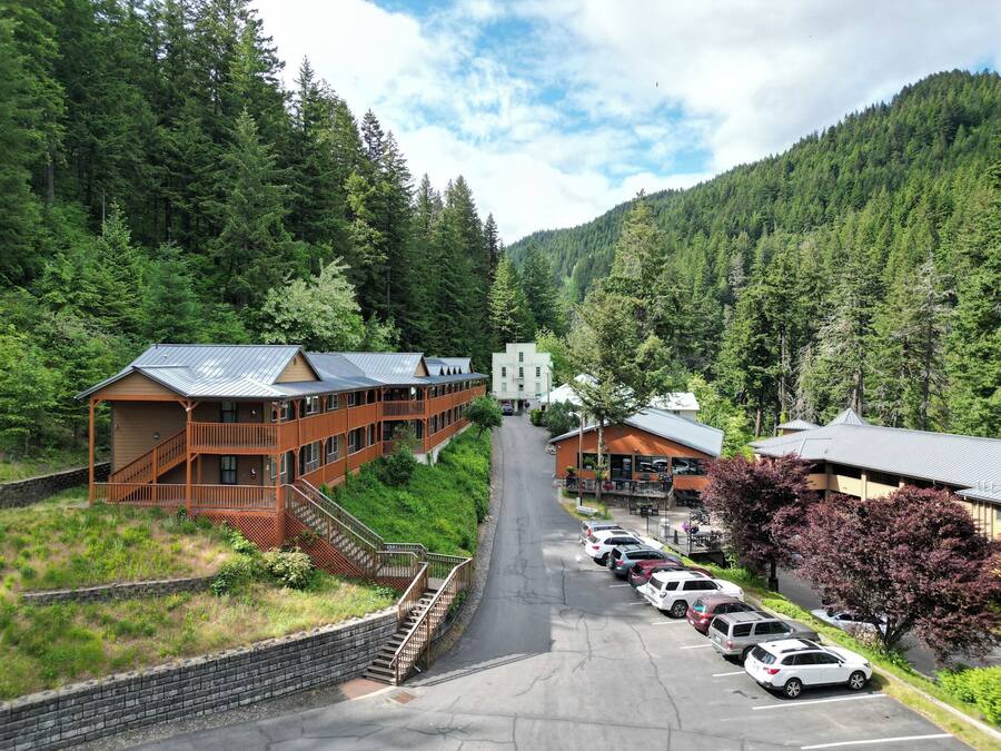 A lodge with a central building and a smaller annex, surrounded by a forested mountain backdrop.