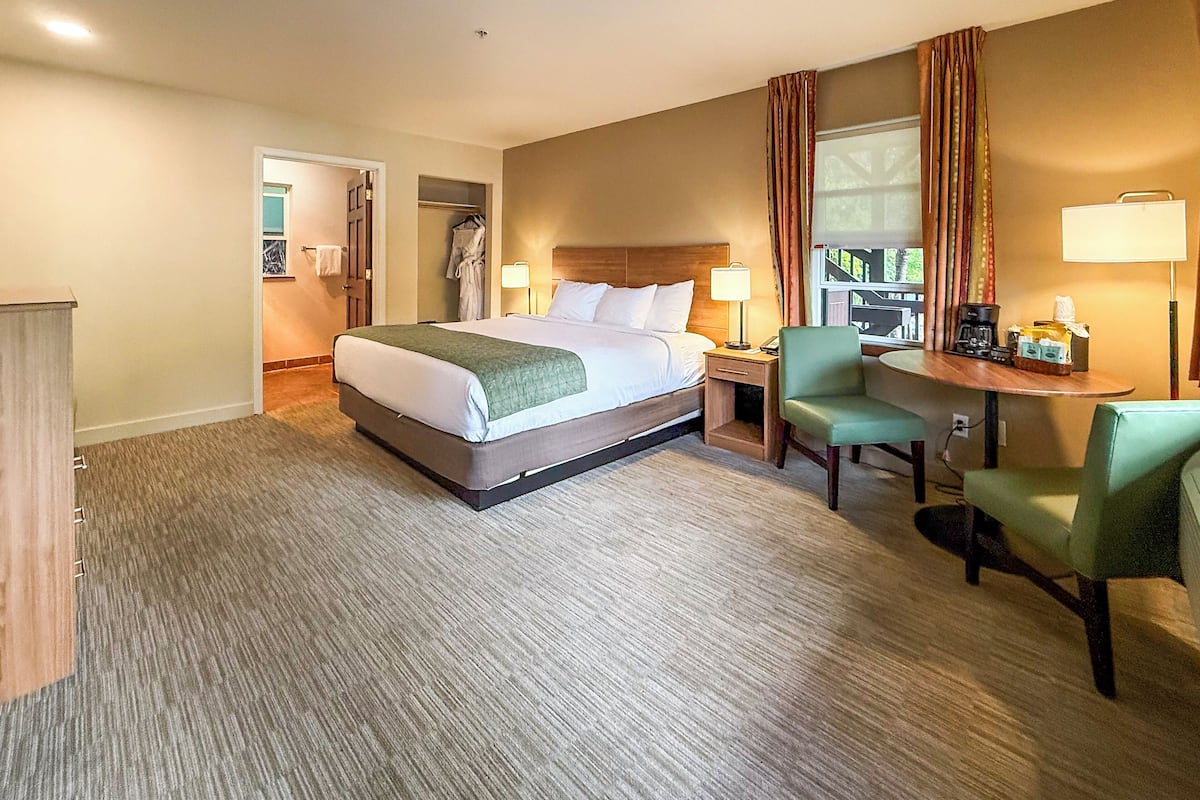 A hotel room with a large bed, a desk with a chair, a lamp, and a window with curtains.