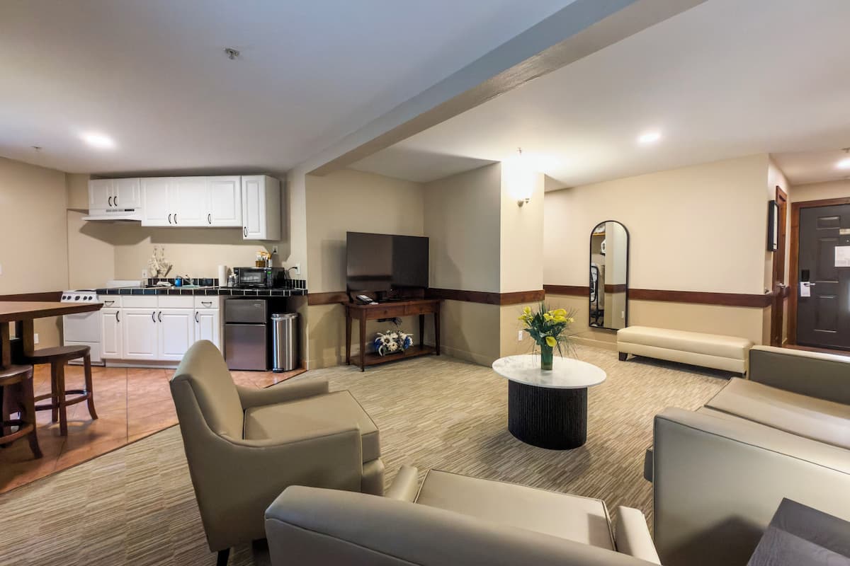 A modern hotel room with a kitchenette, a flat-screen TV, a sofa, and a coffee table.