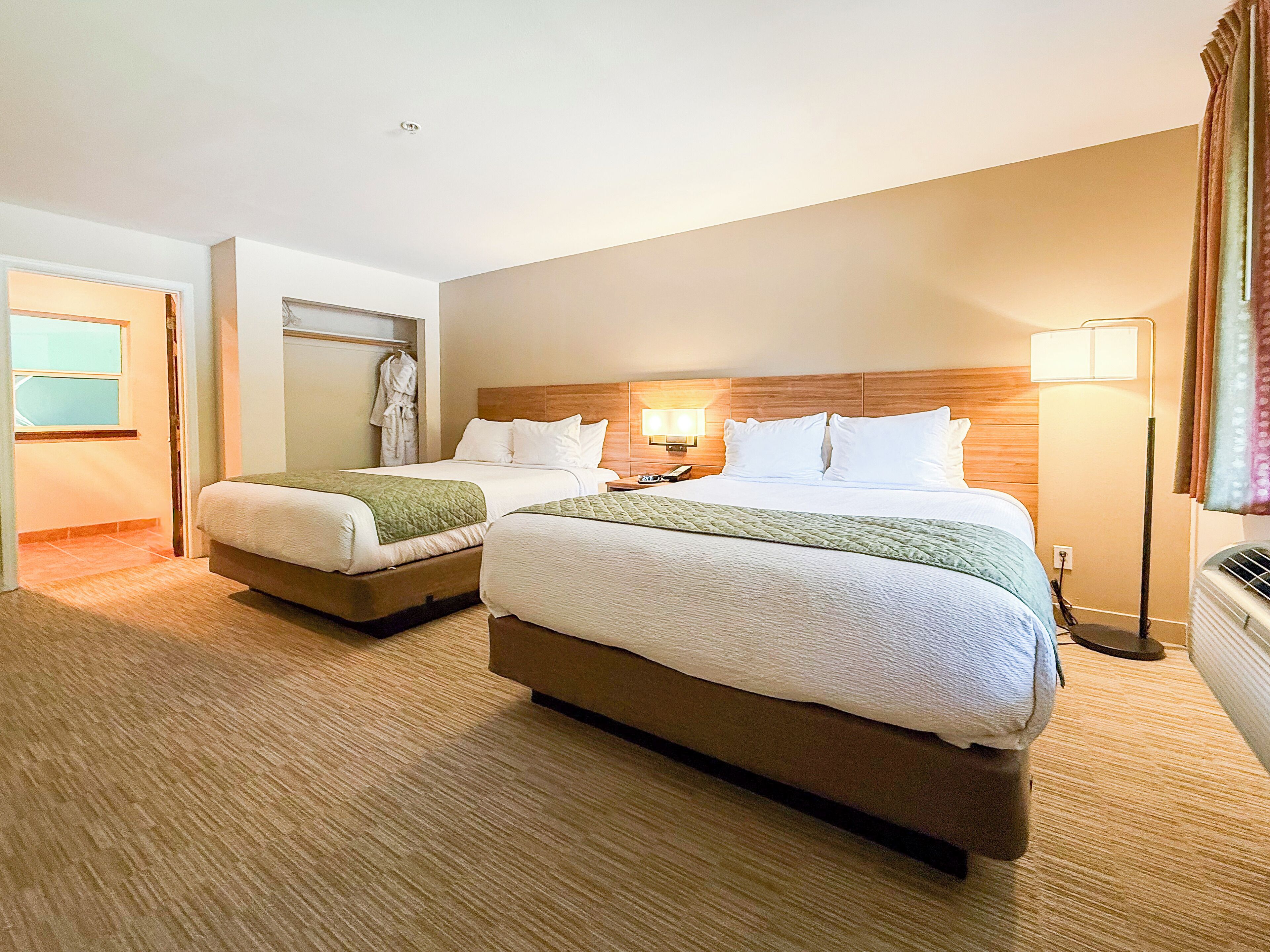 A hotel room with two beds, a robe rack, and a nightstand with a lamp.