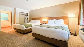 A hotel room with two beds, a robe rack, and a nightstand with a lamp.