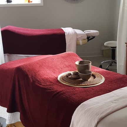 A room with two massage tables covered in red towels, a small window, and a decorative wall piece.
