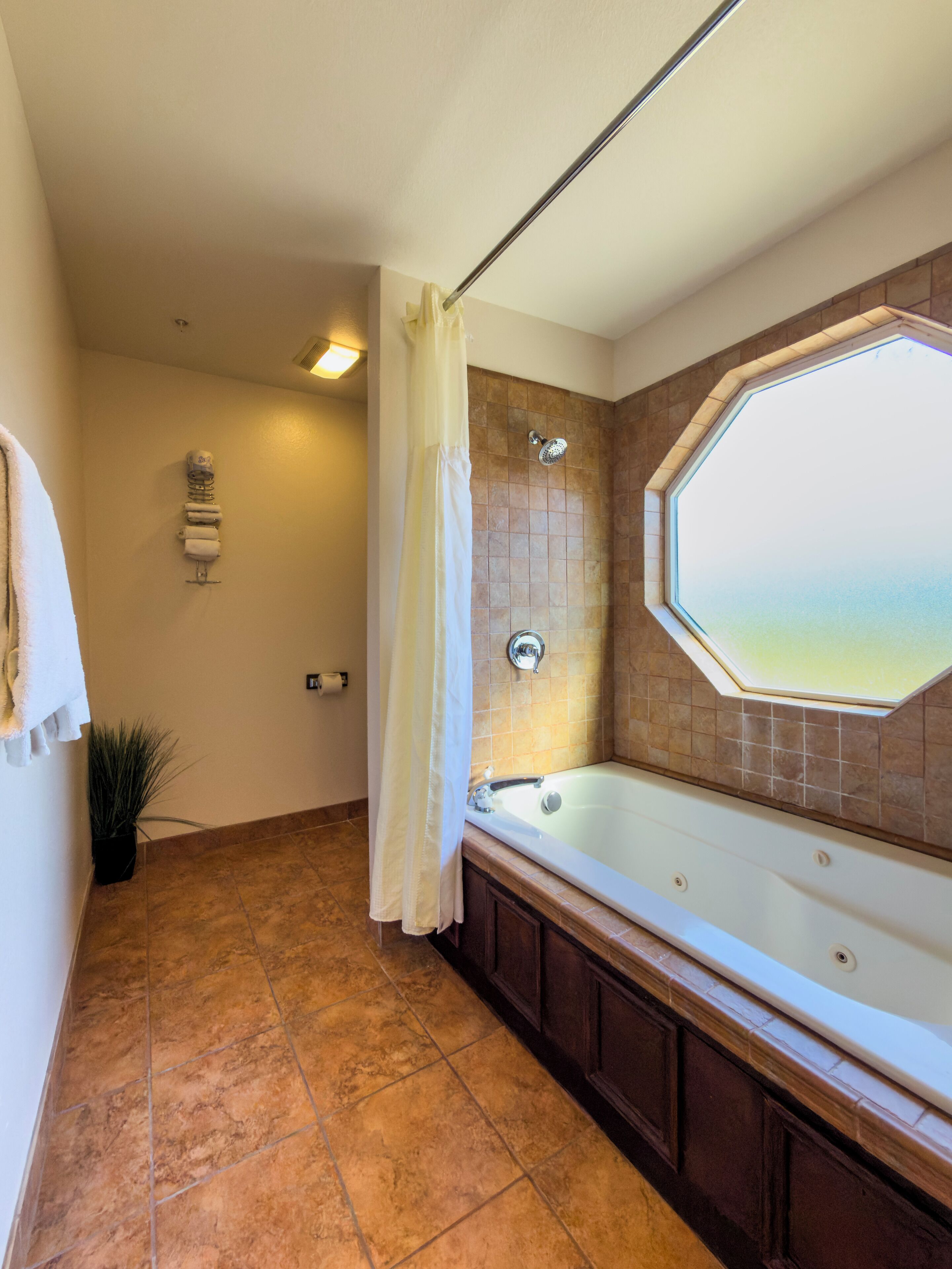 A bathroom with a large bathtub, a shower with a curtain, and a window with a view.