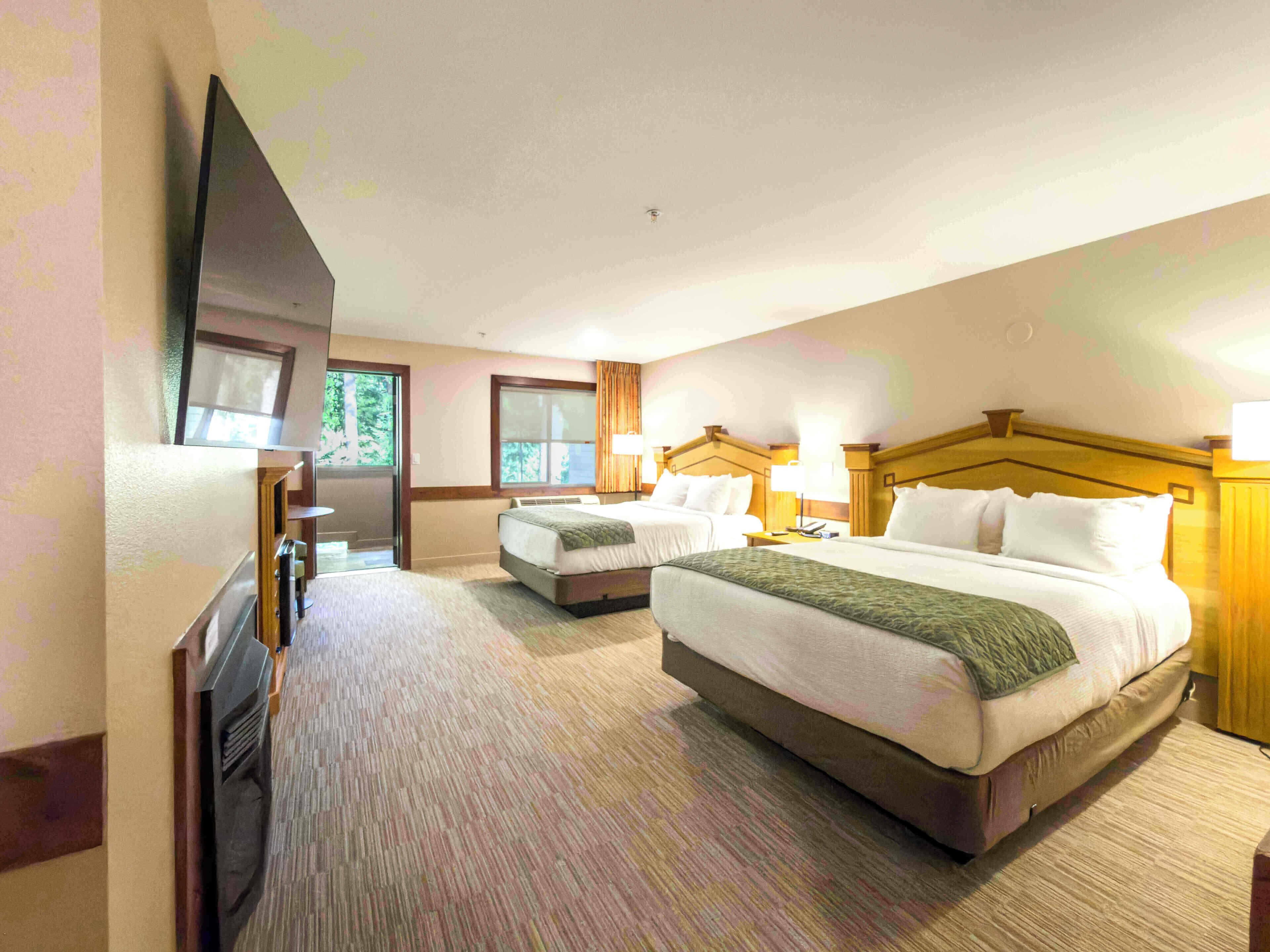 A hotel room with two beds, a TV, and a large window.