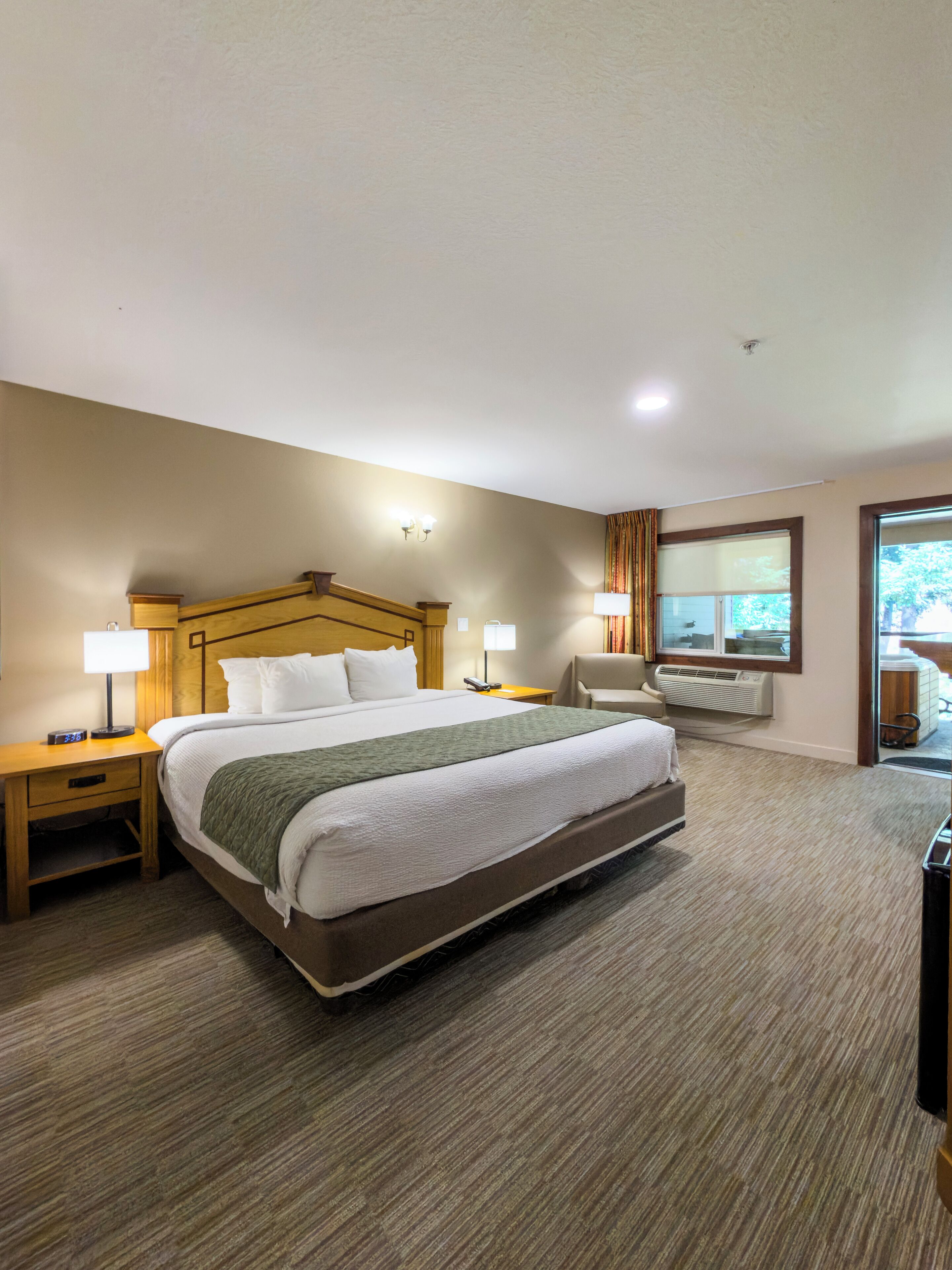 Habitación de hotel con una cama grande, una mesita de noche con lámpara, una silla y una ventana con cortinas.