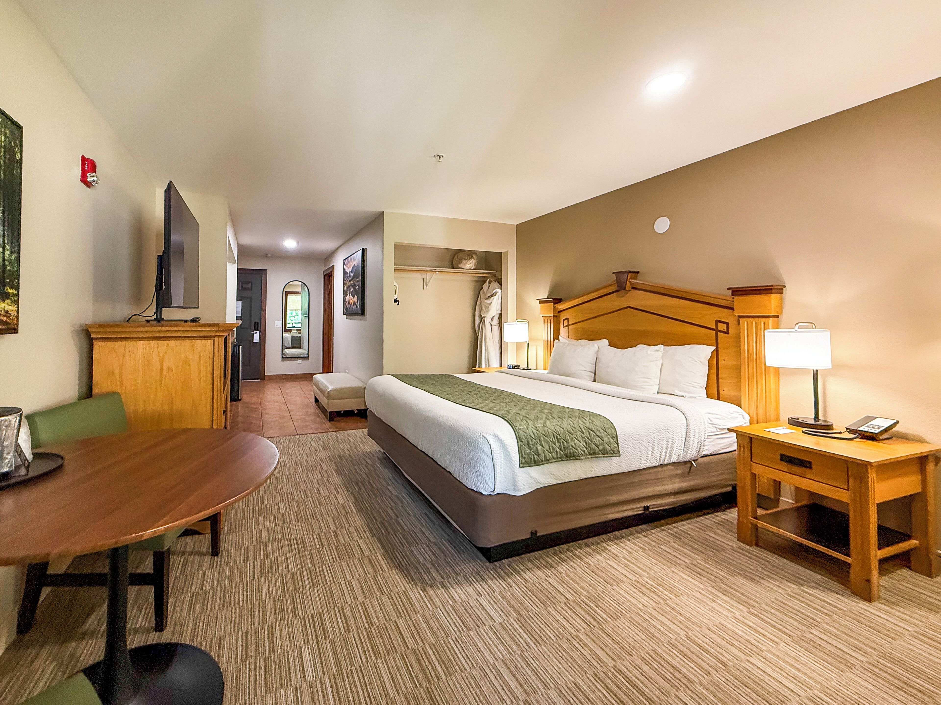 A hotel room with a bed, bedside table, lamp, and a desk with a chair.