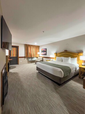A hotel room with a large bed, two bedside tables, a flat-screen TV mounted on the wall, a door with curtains, and a carpeted floor.