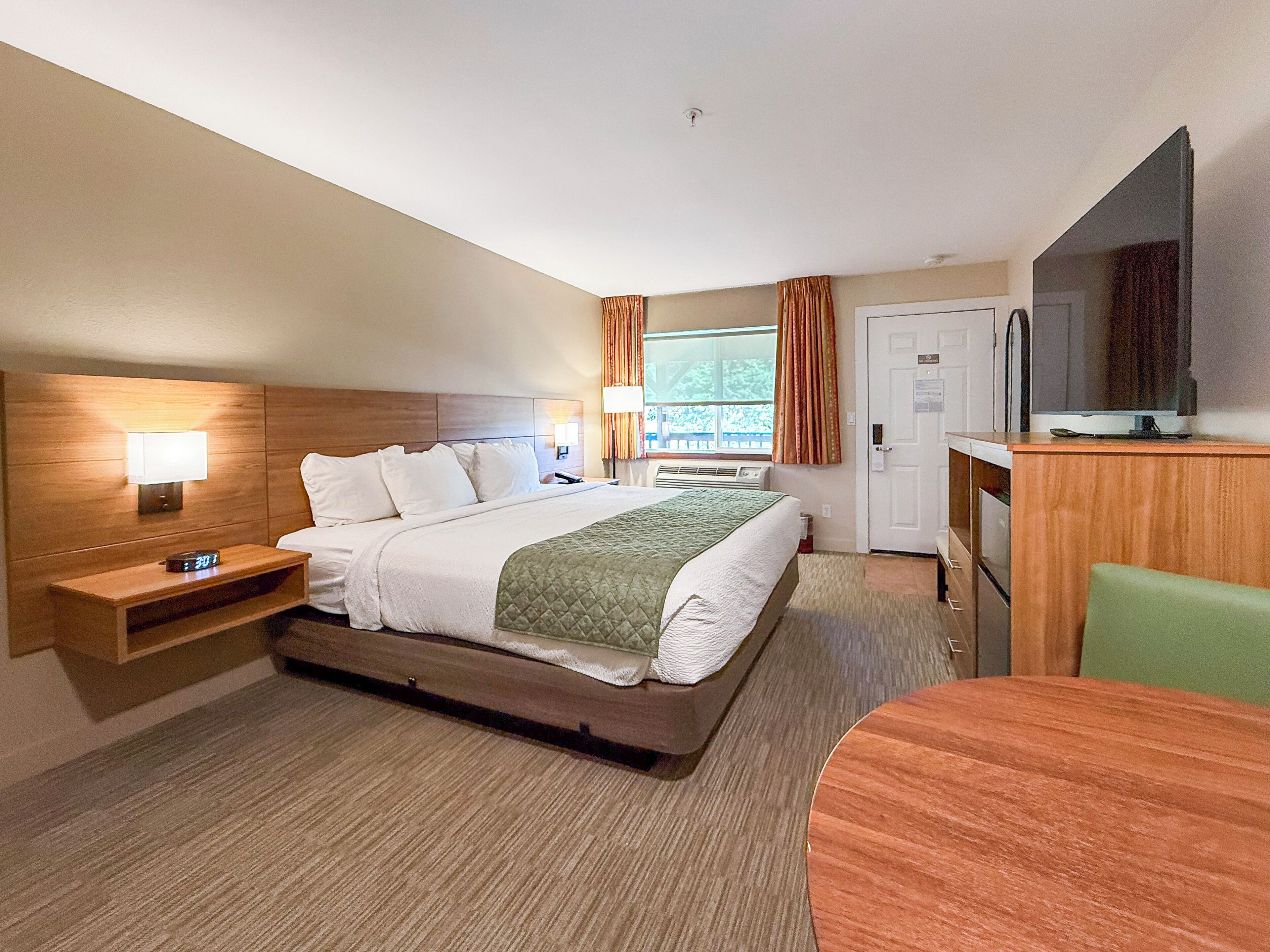 A hotel room with a bed, bedside table, lamp, TV, and a small desk area.