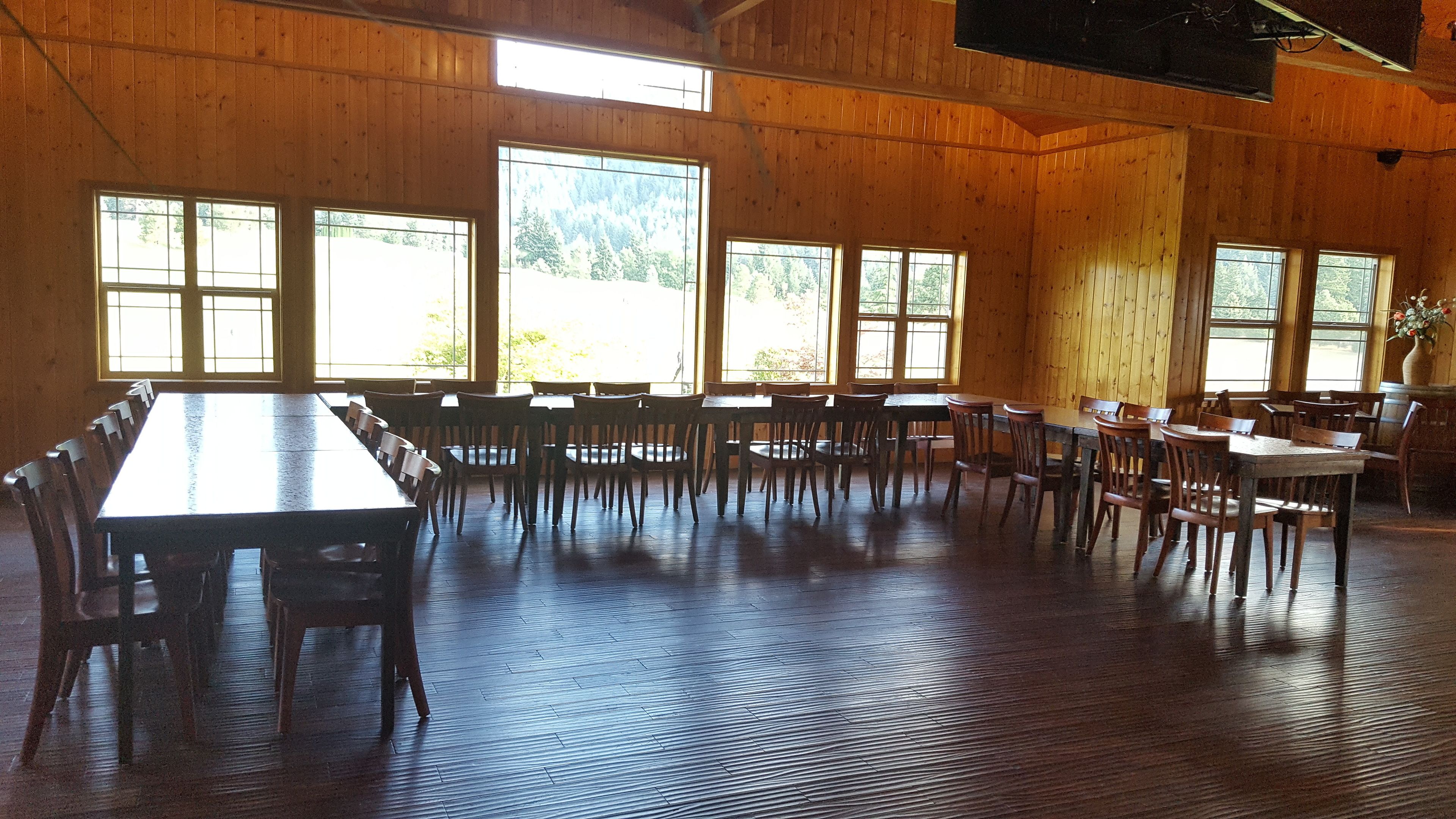A large hall with wooden walls and floors, featuring multiple tables and chairs arranged for dining or meetings.