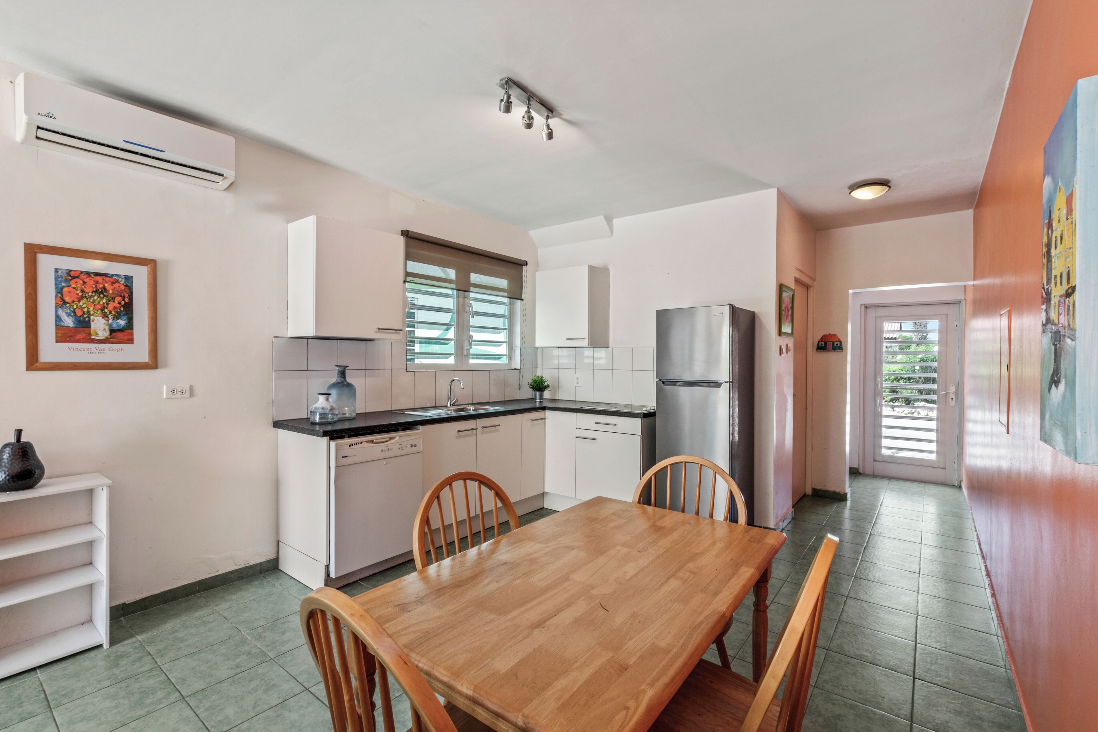 A compact kitchen with white cabinets, a wooden dining table, and a refrigerator.