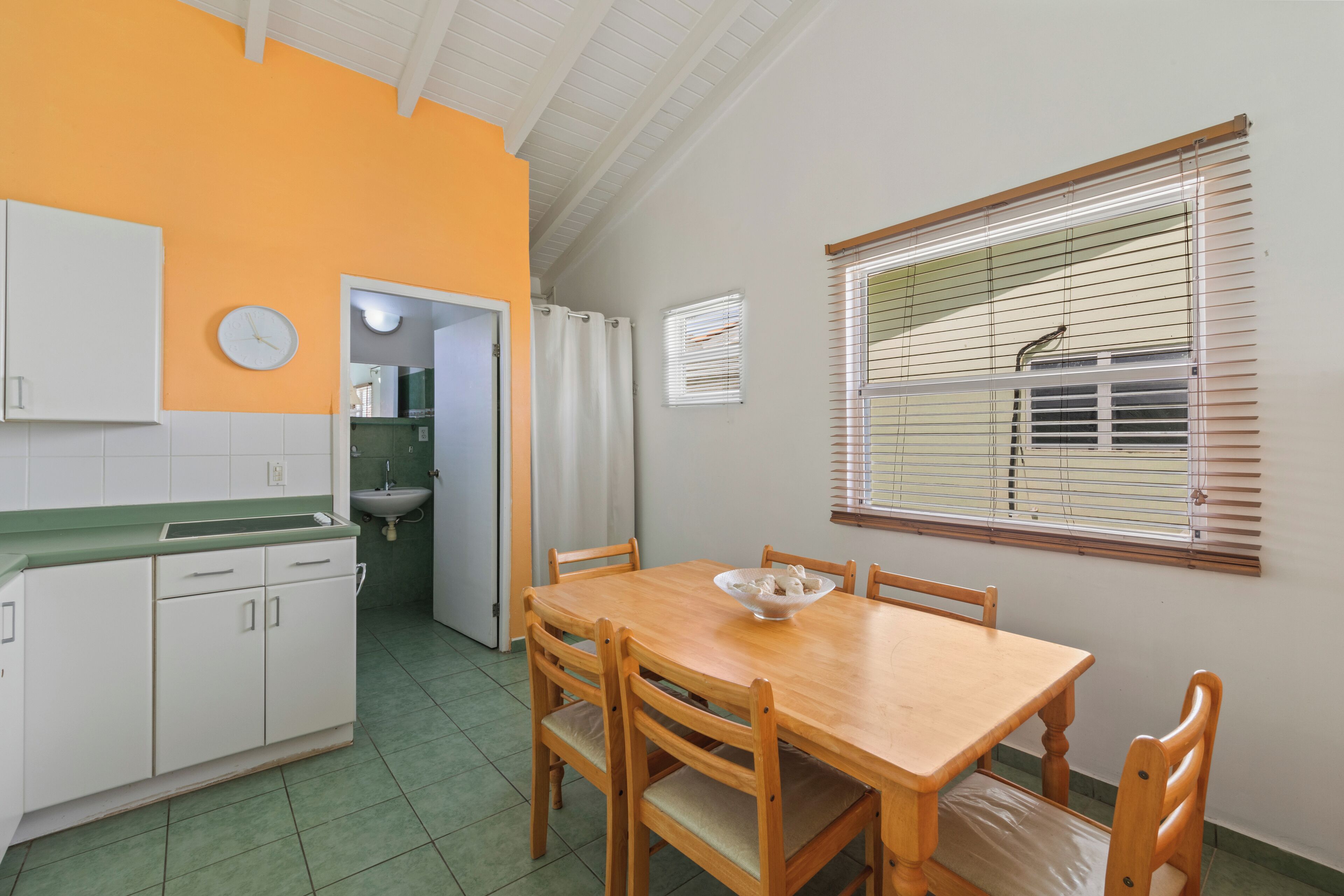 Una cocina compacta con zona de comedor, que incluye una mesa y sillas de madera, un lavamanos y un reloj en la pared.