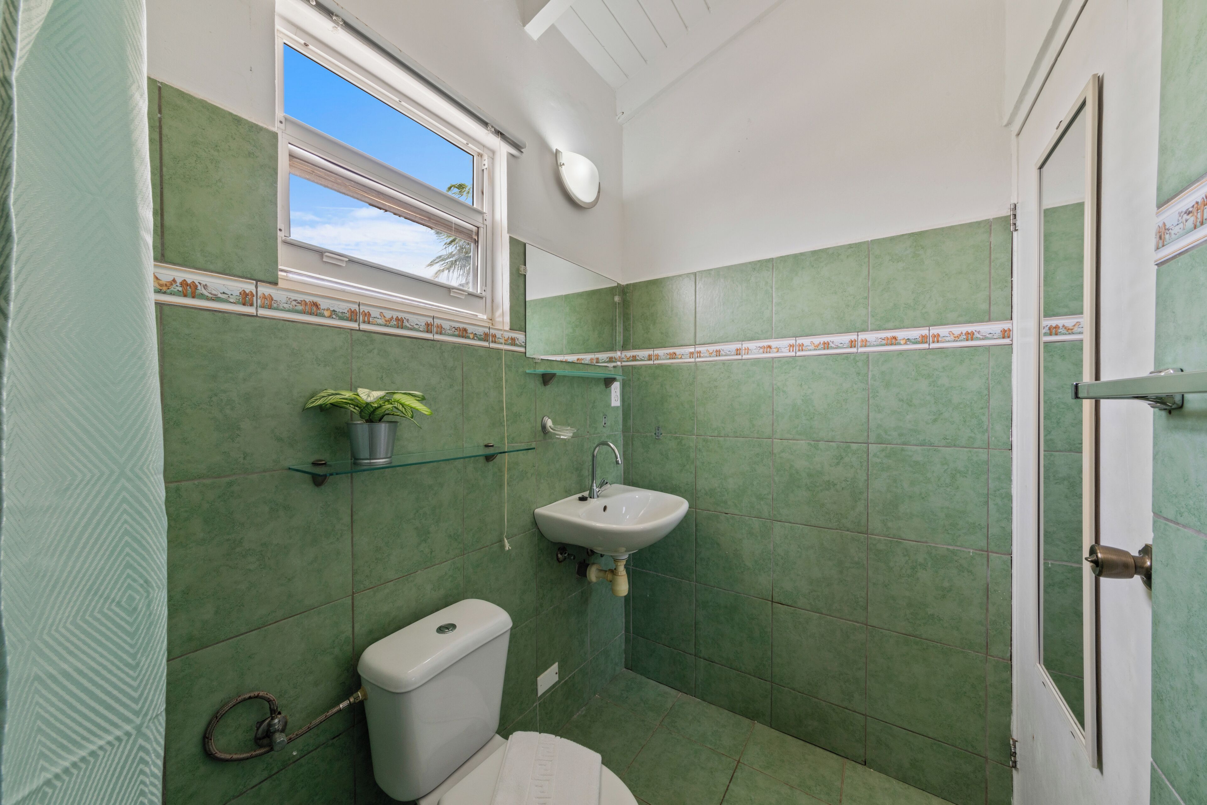 Ein Badezimmer mit grünen Fliesen, einer Toilette, einem Waschbecken, einem Fenster und einer Tür.
