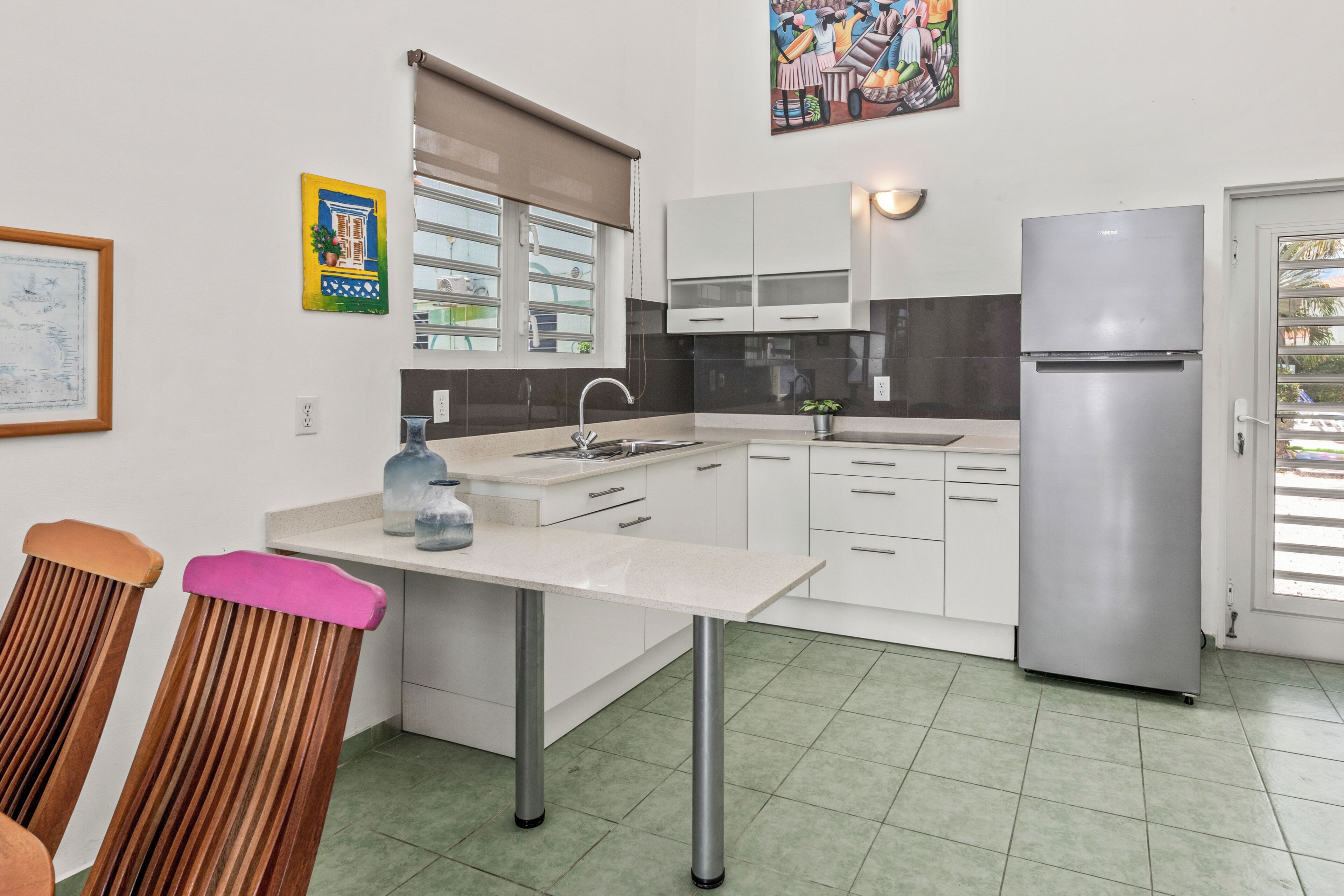Una cocina moderna con armarios blancos, un refrigerador de acero inoxidable y un comedor con sillas de madera.