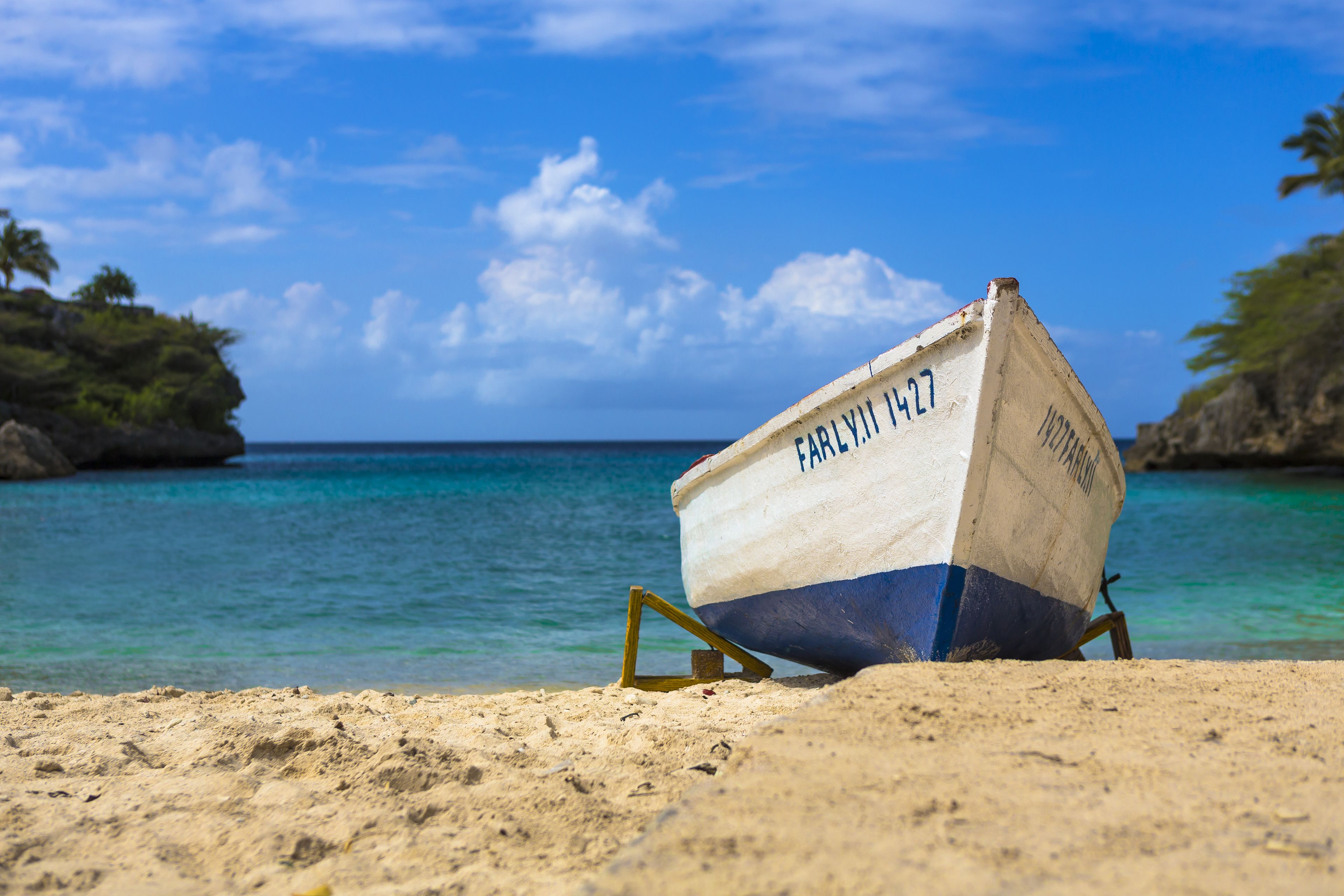 Un bateau portant le numéro 427 est échoué sur une plage de sable fin, avec une eau d’un bleu limpide et une côte rocheuse en arrière-plan.