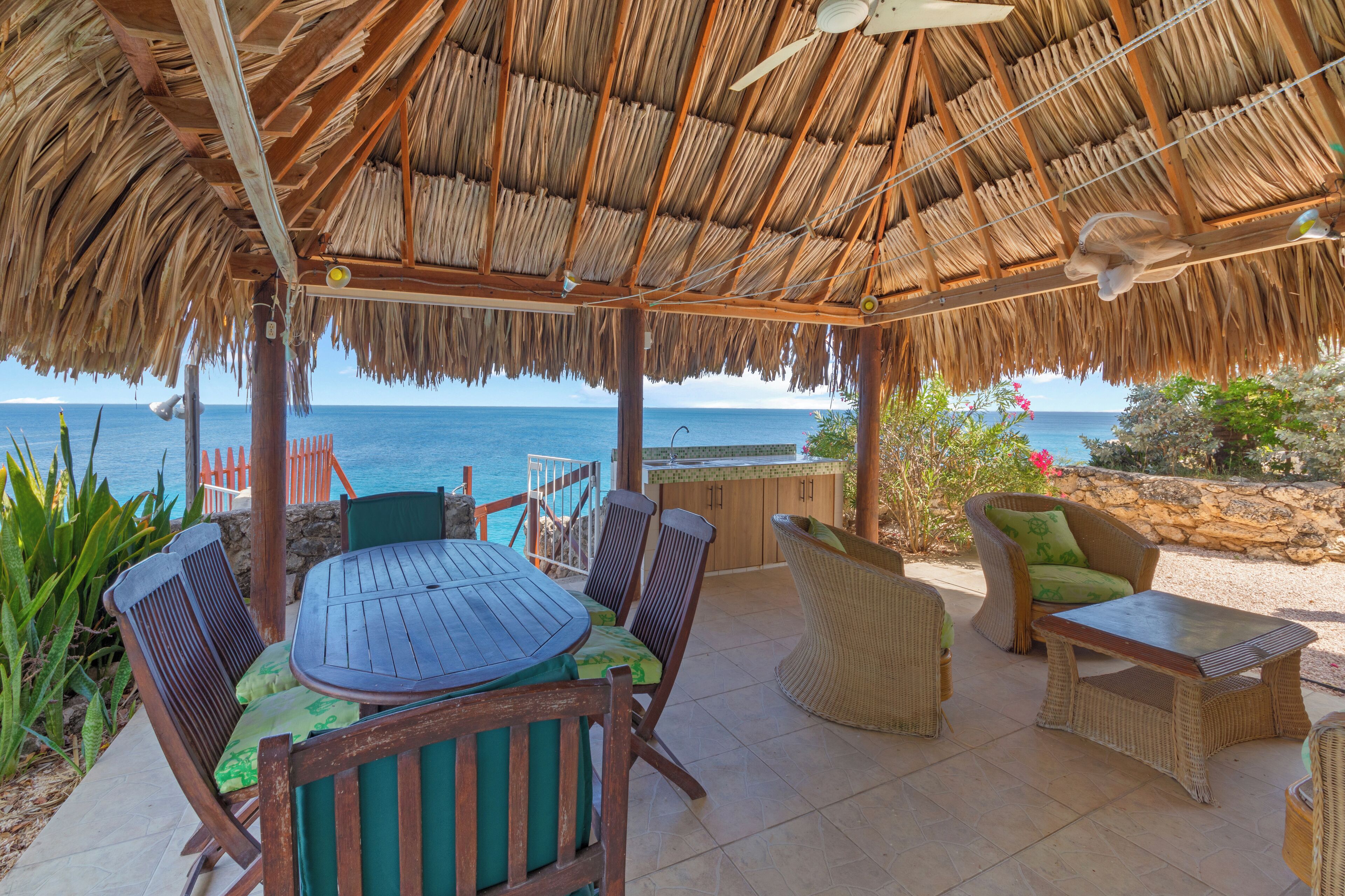 A covered outdoor seating area with a table and chairs, overlooking the ocean.