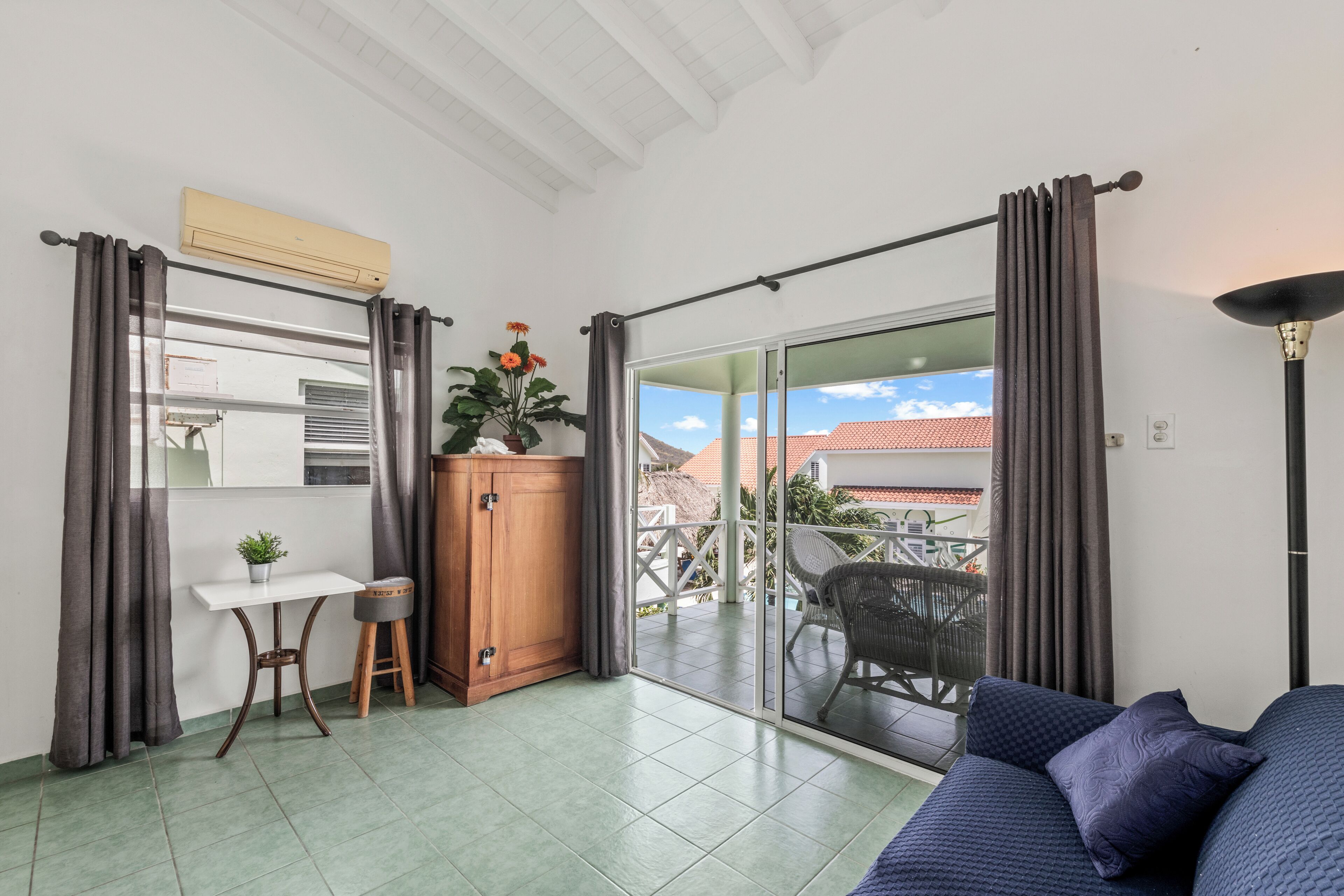 Una habitación con balcón, un sofá, una mesita con una planta, un armario y un ventilador de techo.