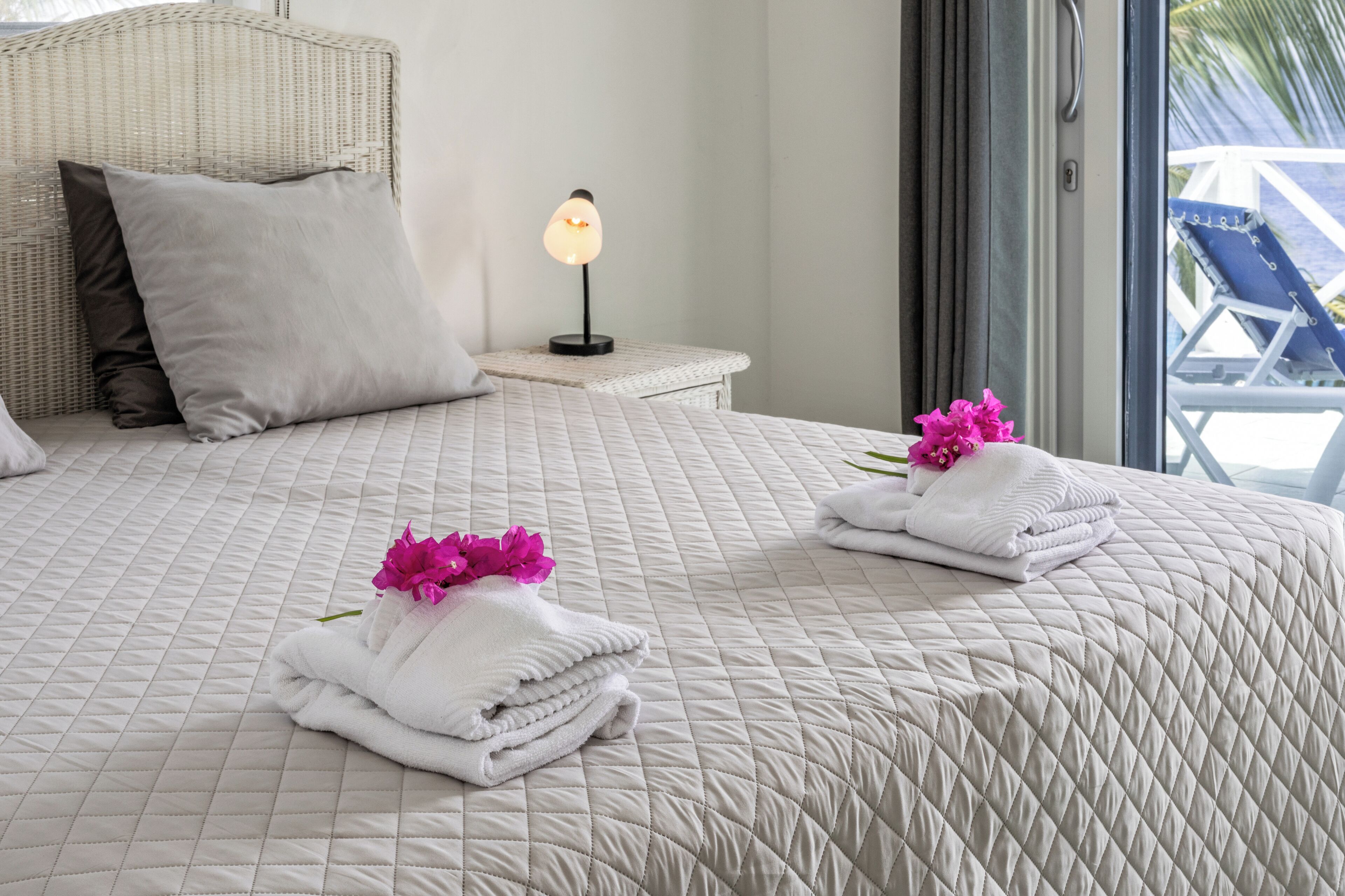 A neatly made bed with a quilted bedspread, pillows, and folded towels with pink flowers.