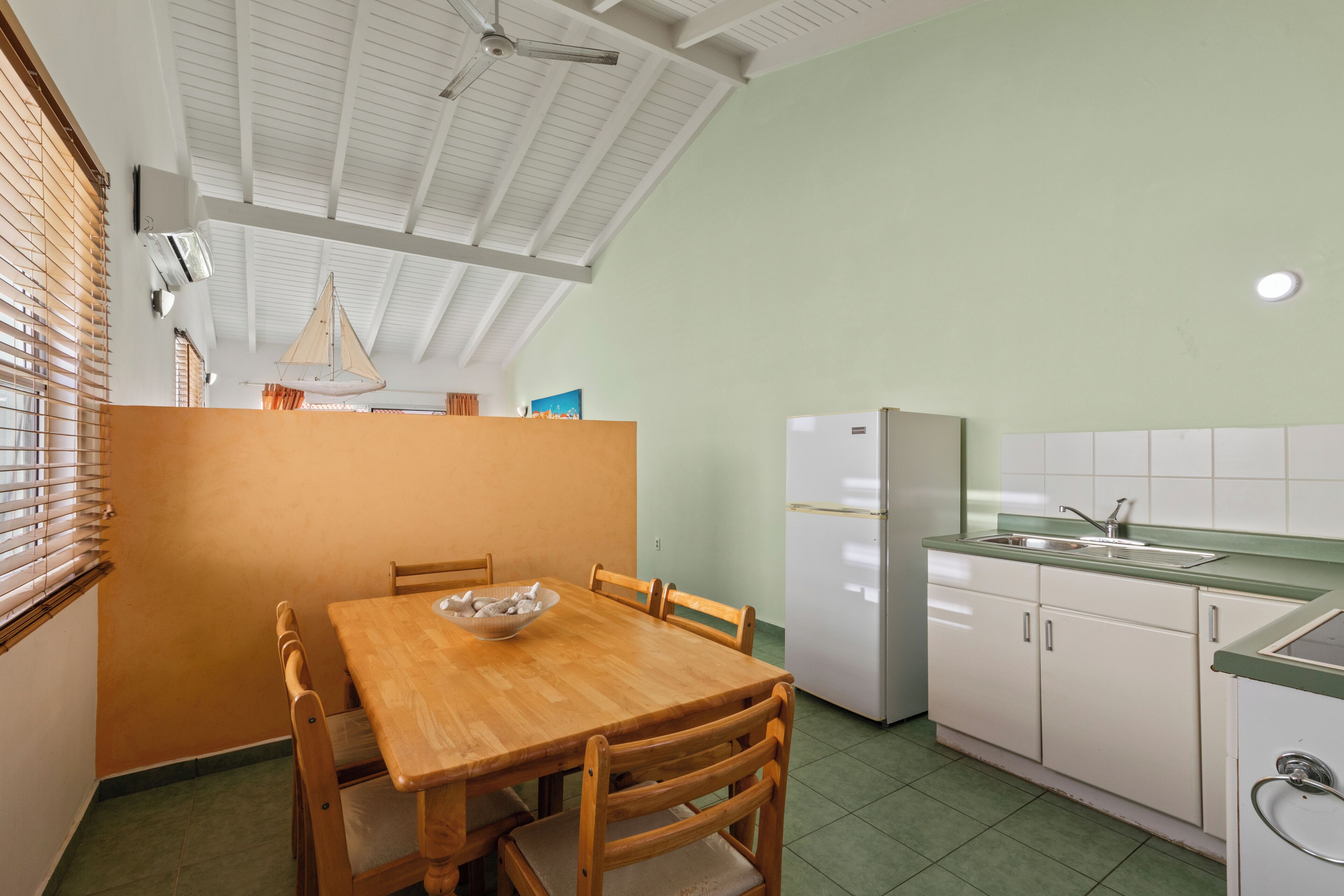 A compact kitchen with a wooden dining table, chairs, a white refrigerator, and a green countertop.