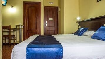 A hotel room with a bed, a desk, and two doors.