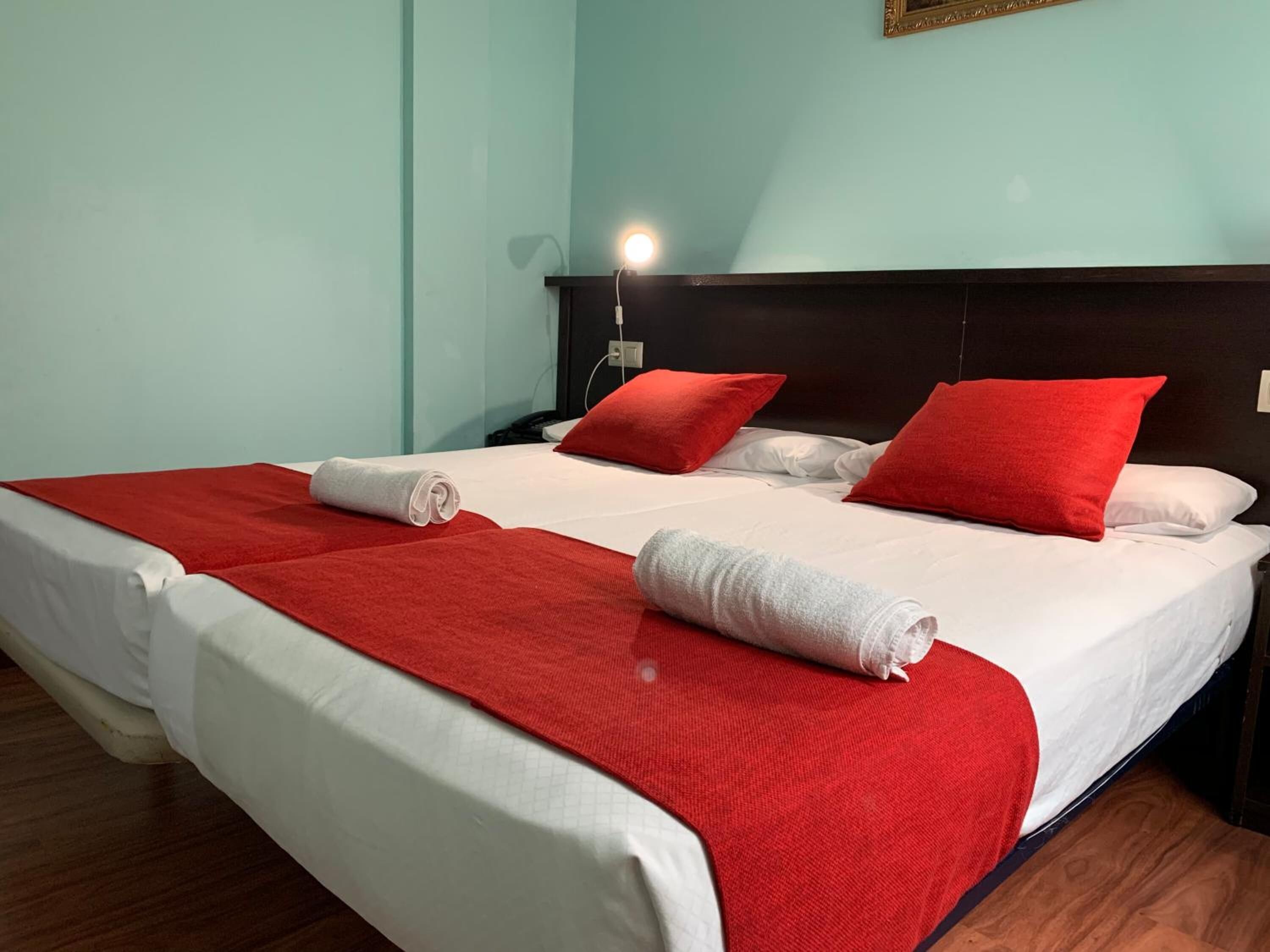 A neatly made bed with red and white bedding, a wooden headboard, and a bedside lamp.