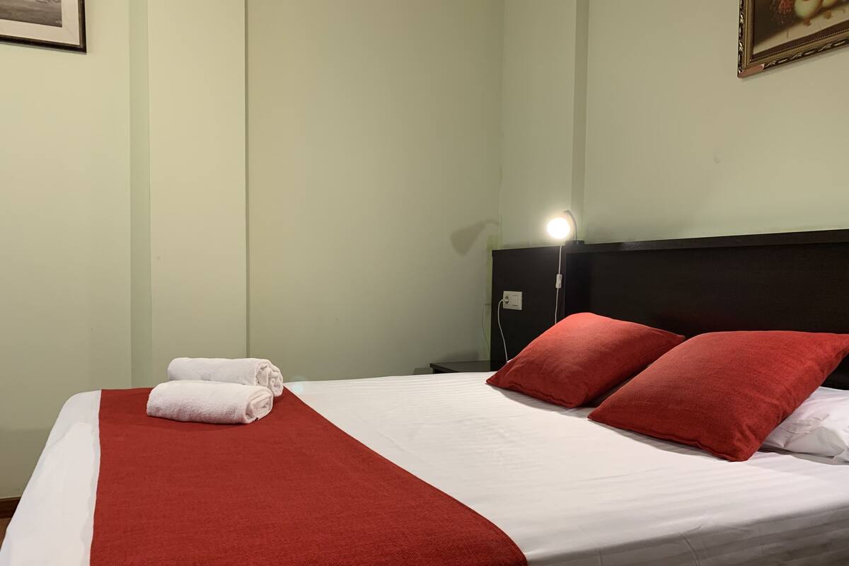 A neatly made bed with white and red linens, a black headboard, and a bedside lamp.