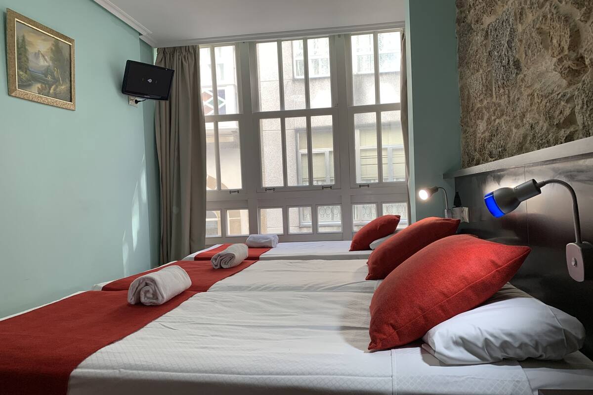 A hotel room with two beds, a large window, a mounted TV, and a desk lamp.