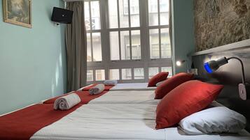 Habitación de hotel con dos camas, un ventanal grande, televisor montado y lámpara de escritorio.
