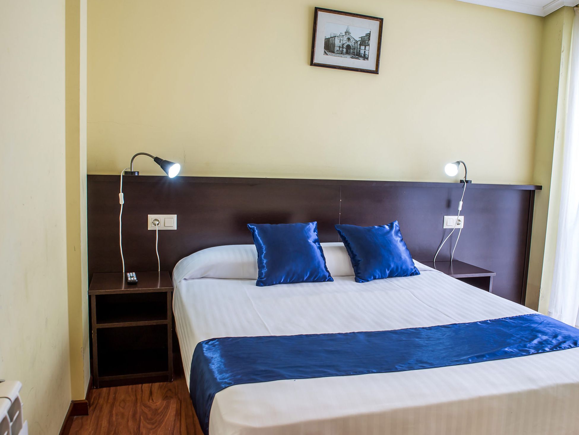 Ein Hotelzimmer mit einem Bett, zwei Nachttischen, einer Lampe und einem gerahmten Bild an der Wand.