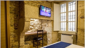 Una habitación con paredes de piedra, una cama, un escritorio y un televisor fijado a la pared.