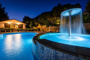 Ein Pool mit Wasserspiel, ein Gebäude mit Dach und Fenstern sowie eine Steinmauer.