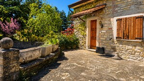 A stone building with a wooden door, a stone wall, and a garden with plants and a stone bench.