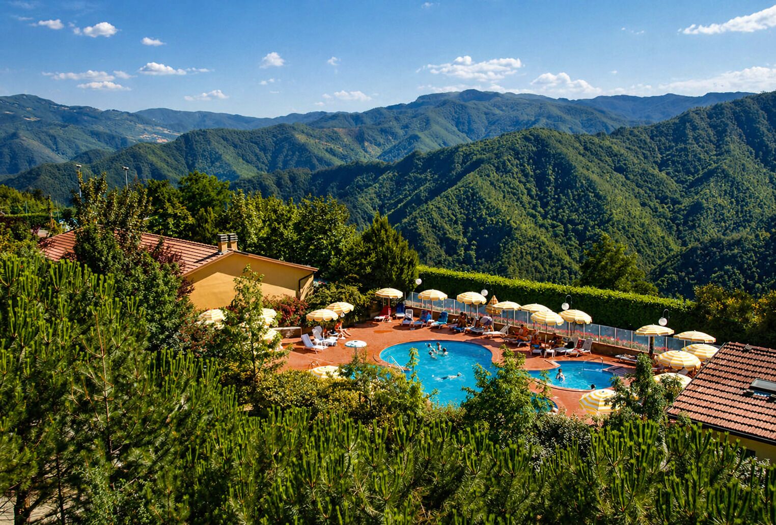 Ein Poolbereich mit mehreren Liegestühlen und Sonnenschirmen, umgeben von üppiger Vegetation und Bergen im Hintergrund.