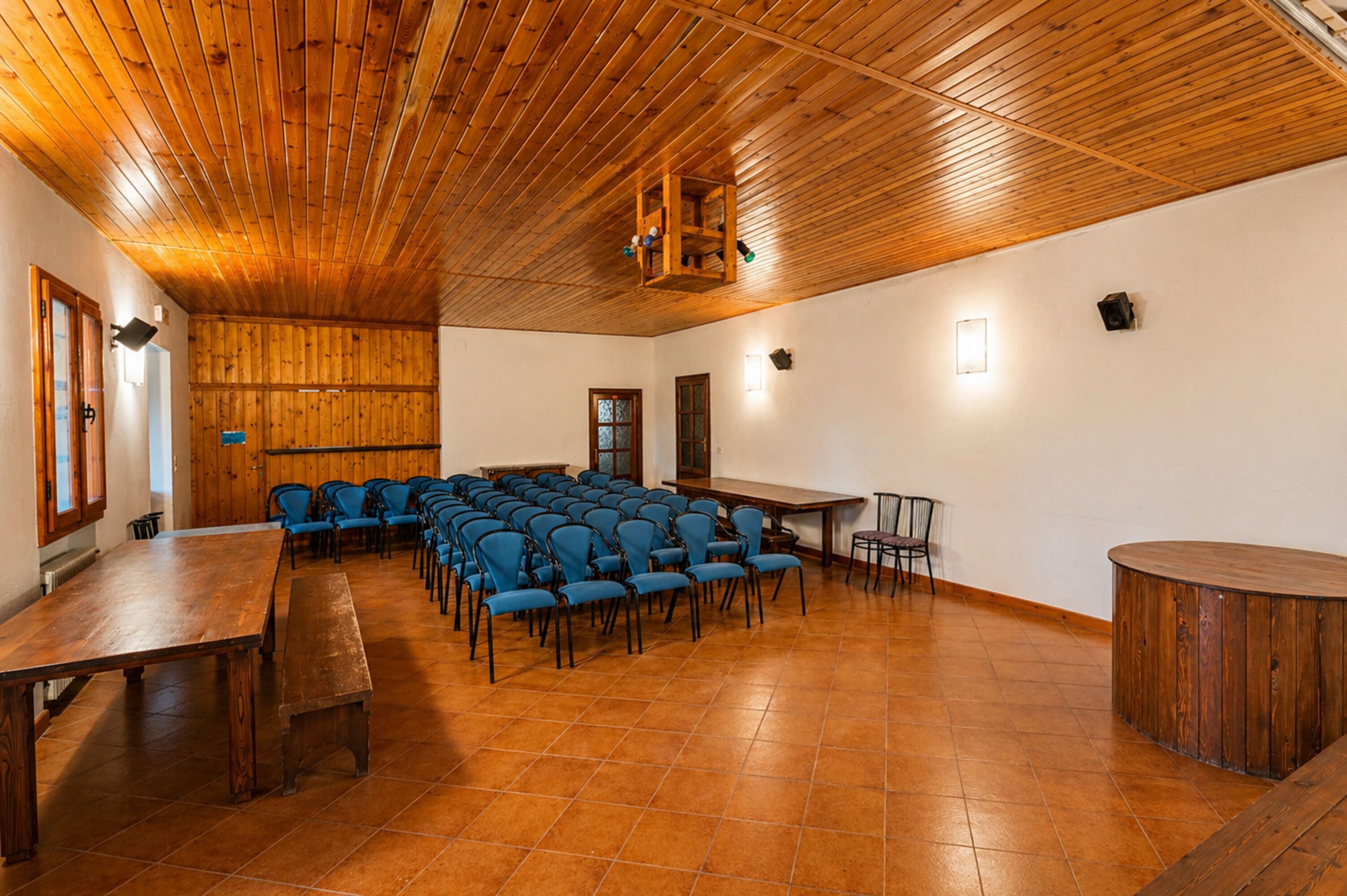Ein Konferenzraum mit Holzbalkendecke, blauen Stühlen, einem langen Tisch und einer Holzbank.