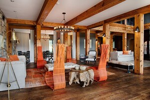 Um quarto espaçoso com vigas de madeira, um lustre grande e um espaço de estar acolhedor com poltronas laranja e um sofá branco.