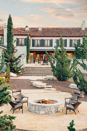 A two-story house with a tiled roof, a stone fire pit, and outdoor seating.