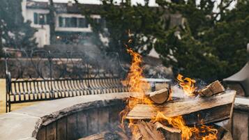 A fire pit with burning logs, surrounded by a stone bench and metal railing.