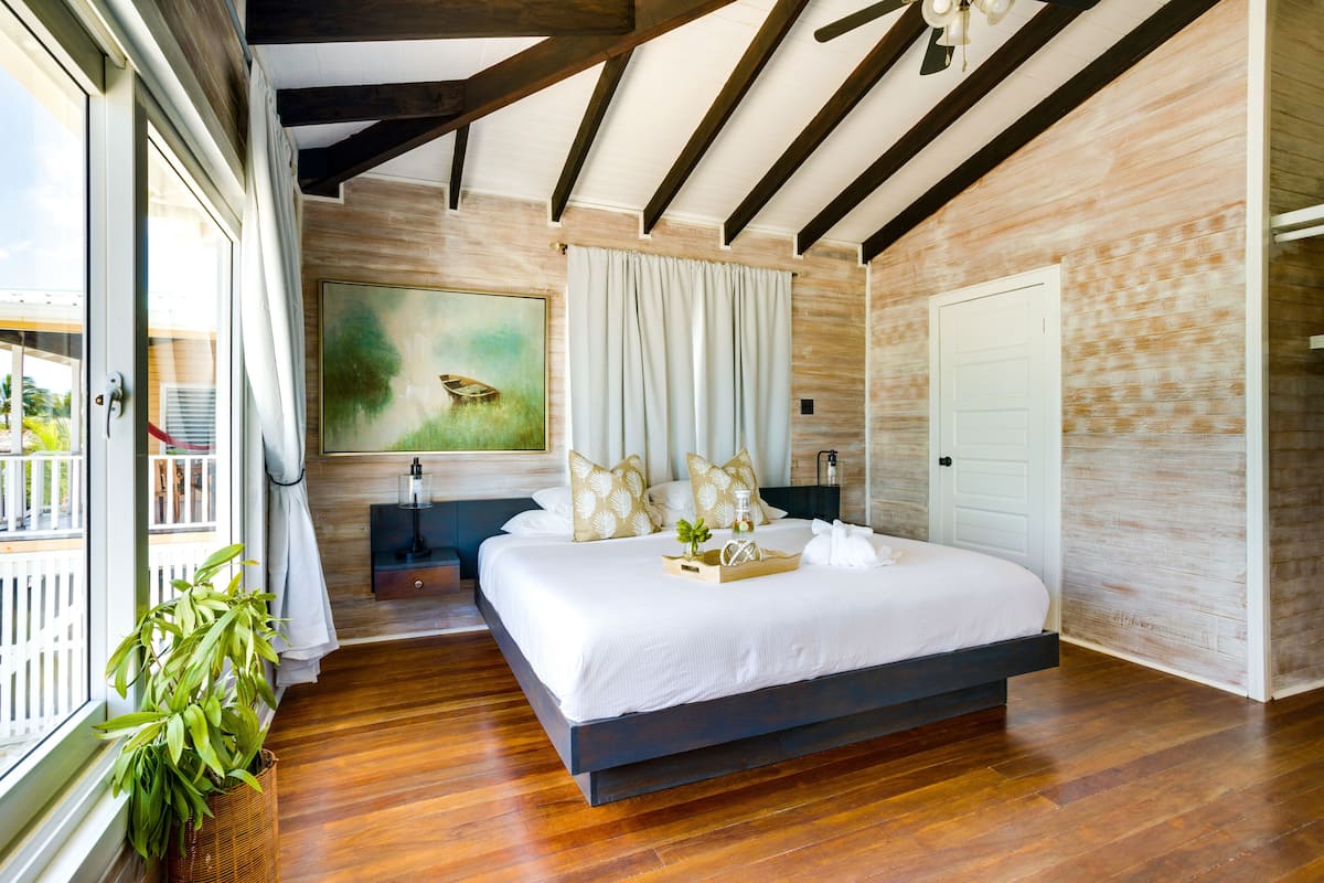 Een moderne slaapkamer met een groot bed, houten balken, een schilderij en uitzicht op het landschap.